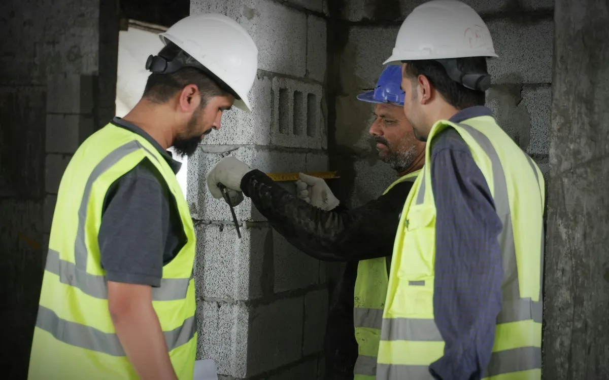 Tres técnicos de obra con casco midiendo con flexómetro un muro de block